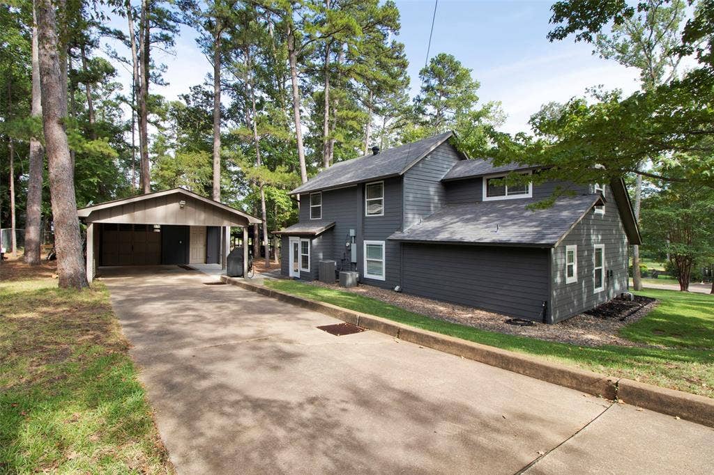 Gray siding exterior with white window trim, mature trees, and a detached carport