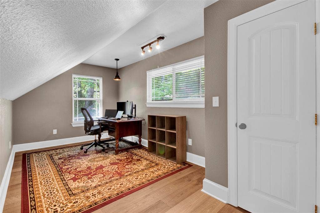 Sloped ceiling room featuring wood-finish flooring, white trim, and a white paneled door