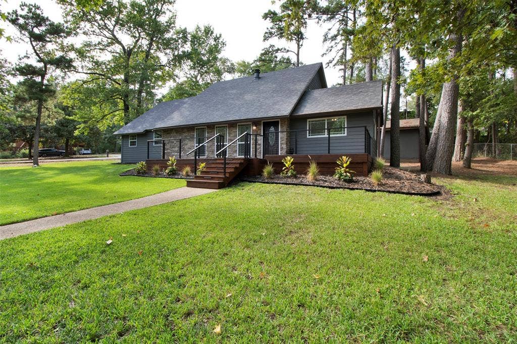 Exterior featuring gray siding, stone accents, a dark shingle roof, a wood-finish deck with dark railings, and a concrete pathway