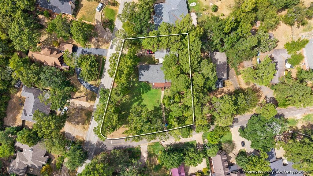 Property with mature trees, a manicured lawn, and an asphalt driveway, situated on a corner lot