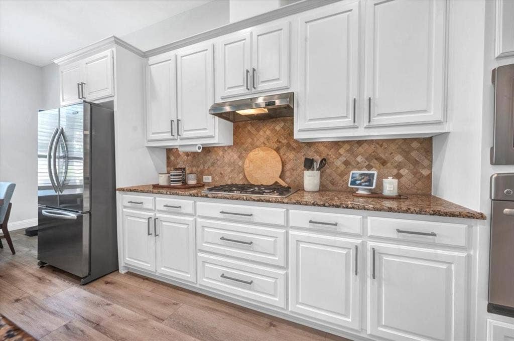 White shaker-style cabinetry with dark hardware, stone countertops, and a full-height backsplash