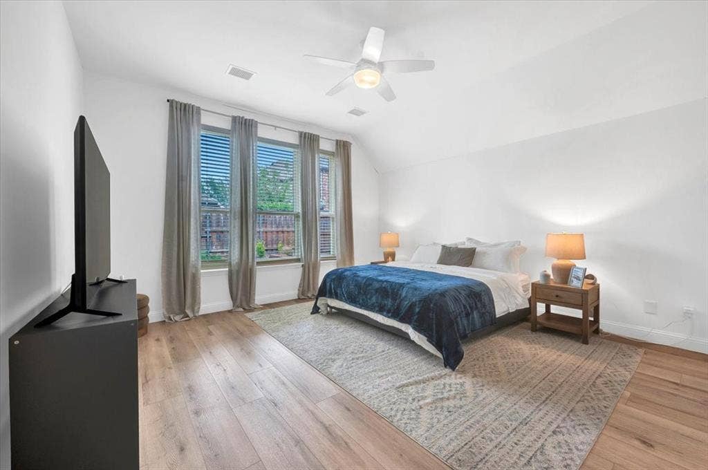 Spacious room featuring wood-finish flooring, a contemporary ceiling fan, and multiple windows with blinds