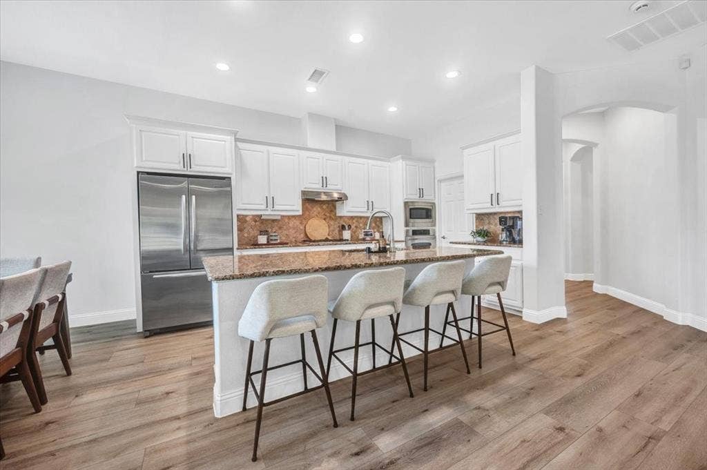Kitchen featuring wood-finish flooring, white cabinetry, a large kitchen island with counter seating, stainless steel appliances, and recessed lighting