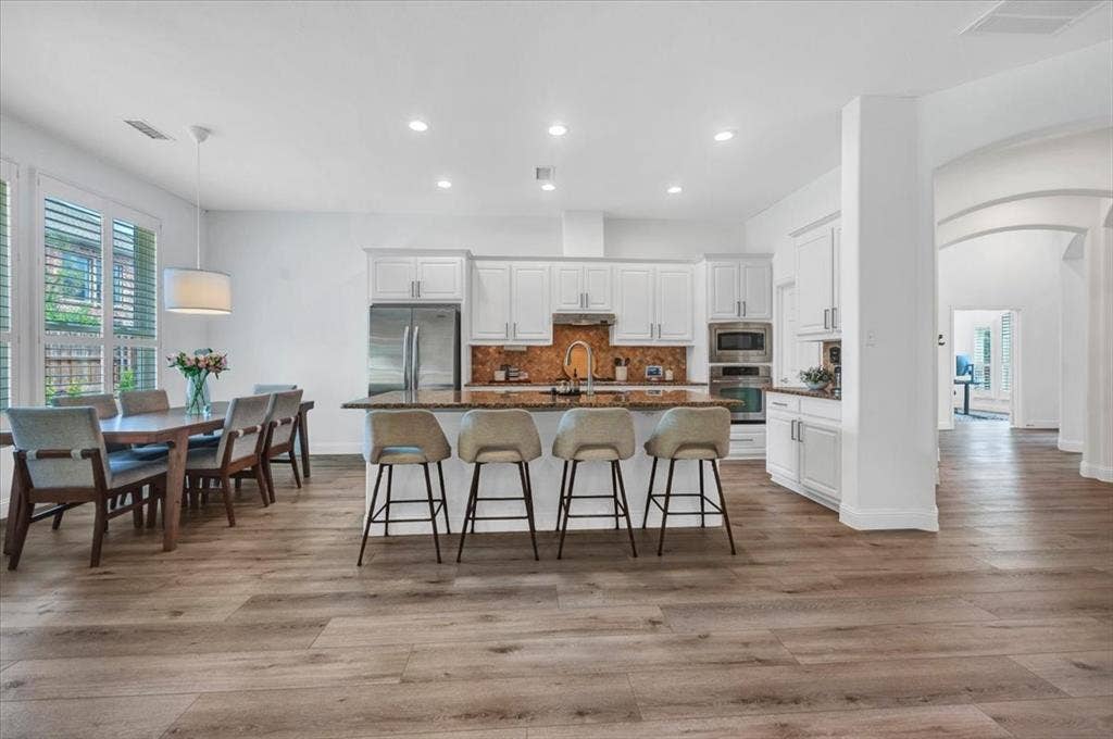 Kitchen island with stone countertop, stainless steel appliances, and wood-finish flooring