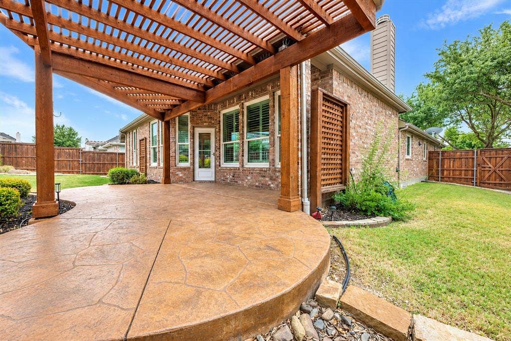 Expansive patio featuring a wood pergola, stamped concrete, brick exterior, and full privacy fencing