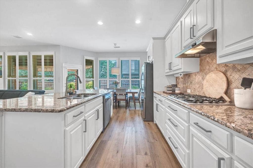 Open-concept kitchen featuring wood-finish flooring, white cabinetry, granite countertops, and a tile backsplash