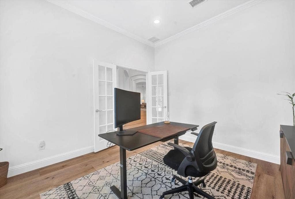 Dedicated home office featuring a wood-finish desk with integrated storage, ergonomic seating, recessed ceiling lighting, and French doors with glass panes opening to adjacent spaces