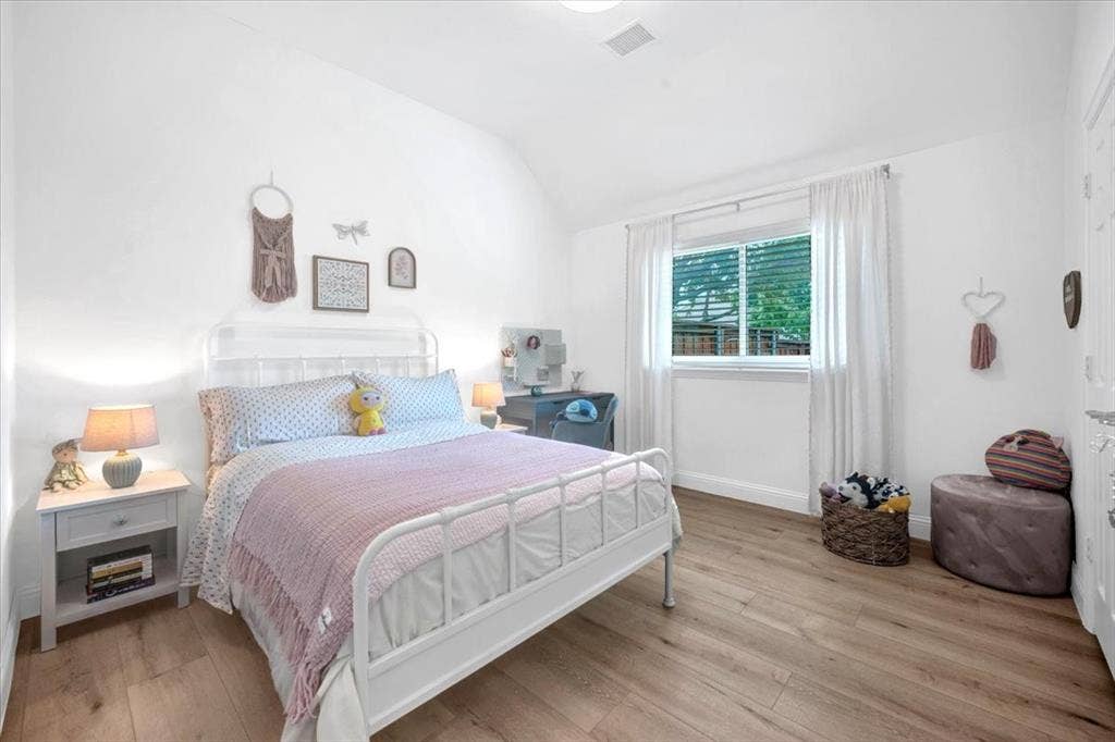 Vaulted ceiling, wood-finish flooring, white walls, and a window with white blinds and curtains
