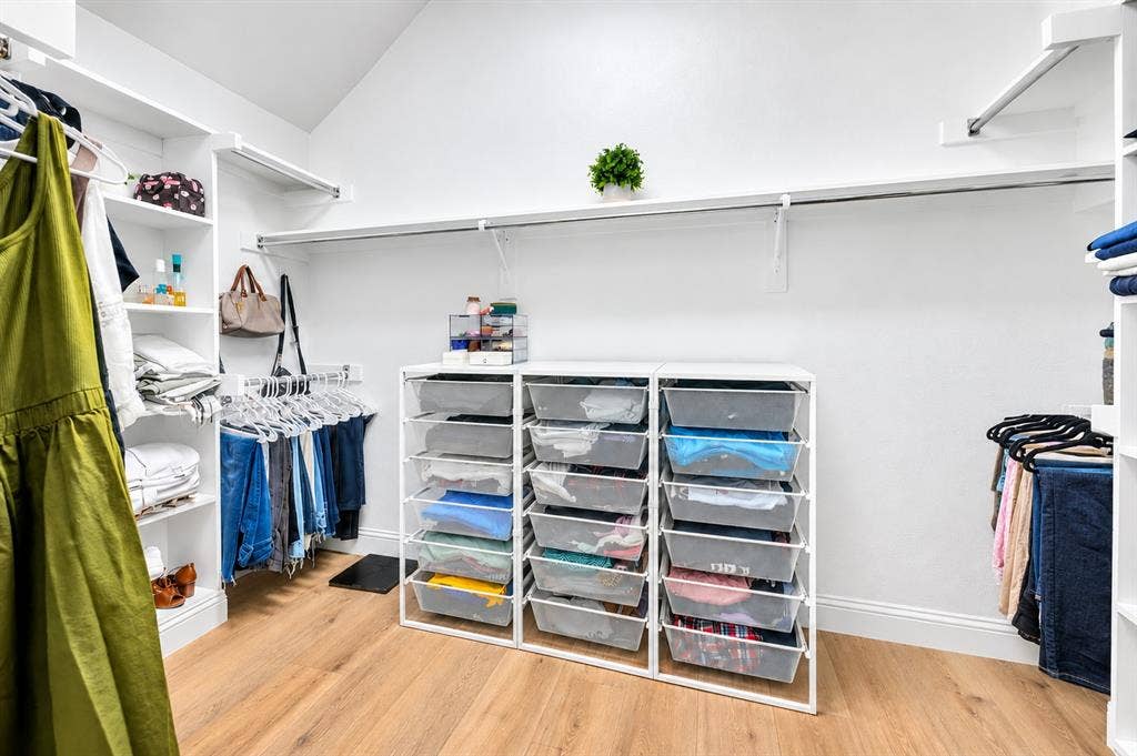 Vaulted ceiling, wood-finish flooring, built-in shelving, white walls, clothes hanging rods
