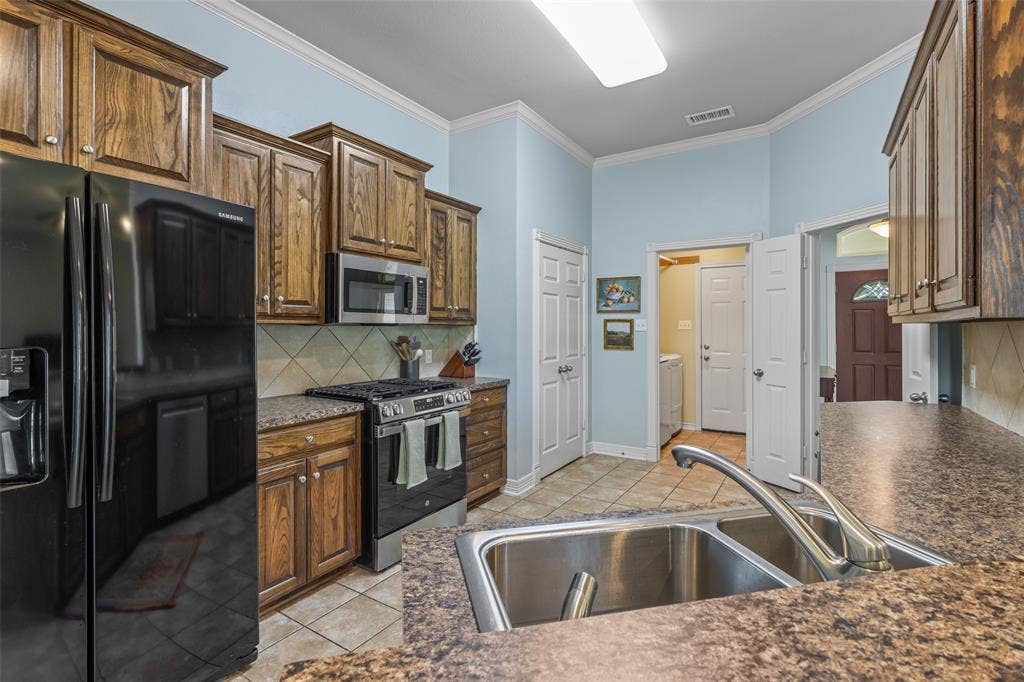 11848 County Road 167, Tyler, TX 75703 Kitchen featuring wood cabinetry, stainless steel appliances, a double basin sink, and tile flooring