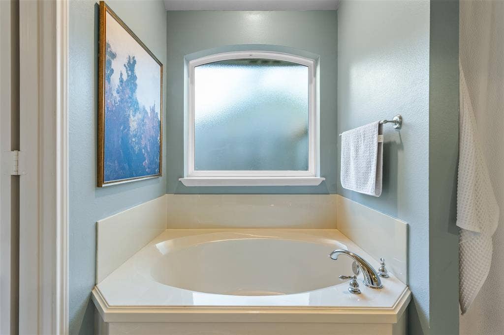 11848 County Road 167, Tyler, TX 75703 Built-in corner soaking tub with deck-mounted chrome fixtures, an arched frosted window, and a surrounding light-toned ledge