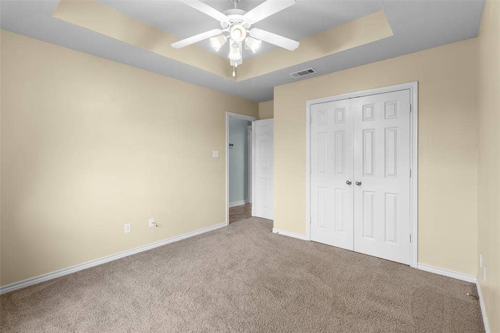 11848 County Road 167, Tyler, TX 75703 Tray ceiling with a ceiling fan, neutral wall paint, white trim, carpeted flooring, and paneled bifold doors