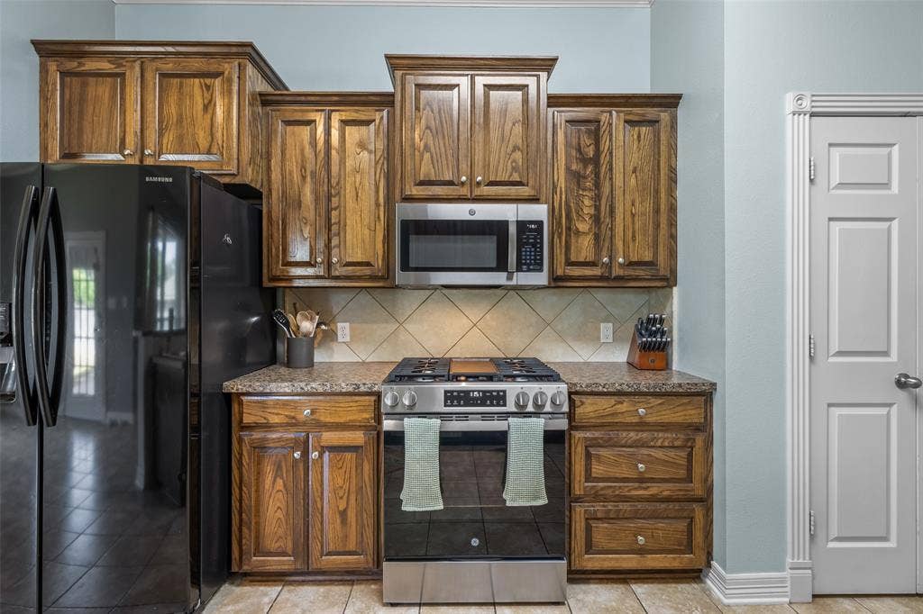 11848 County Road 167, Tyler, TX 75703 Kitchen featuring wood cabinetry, stainless steel range, microwave, and a tile backsplash