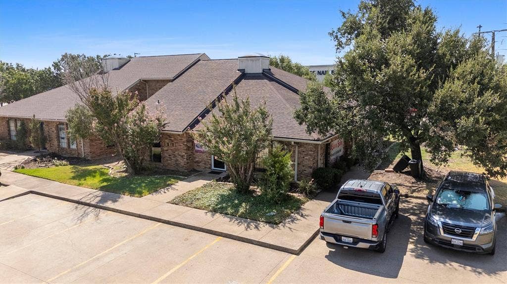 1055 W Pioneer Parkway, Grand Prairie, TX 75051 Brick exterior structure with multiple gables and a shingled roof, featuring mature landscaping and a paved parking area