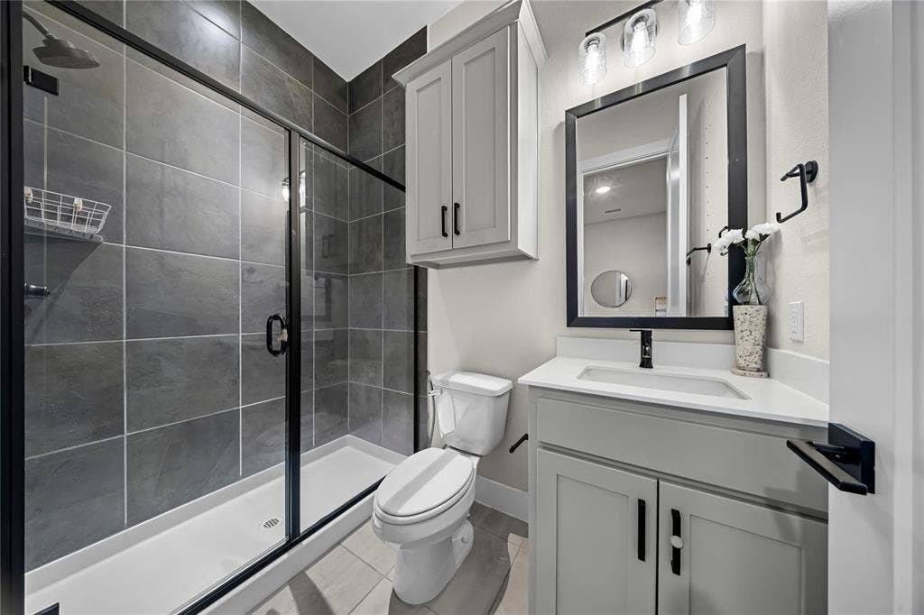 467 Mayfair Lane, Frisco, TX 75033 Walk-in shower with dark tile surround, light gray vanity with white countertop, and framed mirror with integrated lighting