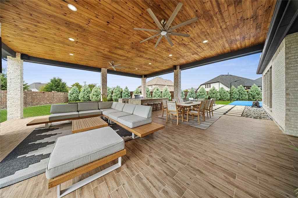 467 Mayfair Lane, Frisco, TX 75033 Expansive covered patio featuring a wood-panel ceiling with recessed lighting and ceiling fans, stone-clad support columns, wood-finish tile flooring, and a built-in outdoor kitchen area