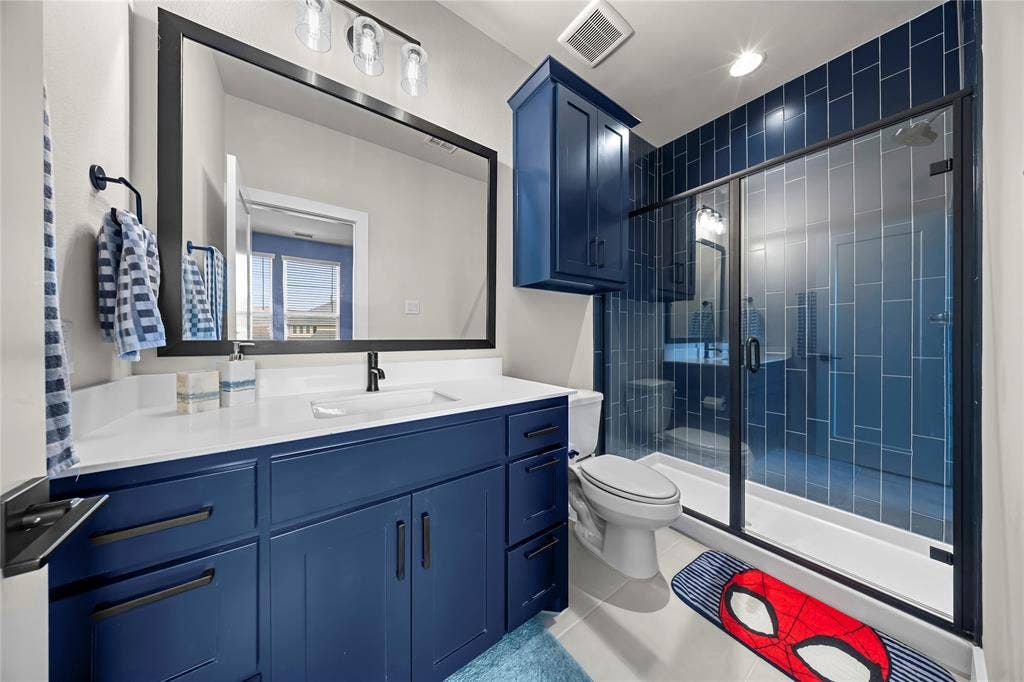 467 Mayfair Lane, Frisco, TX 75033 Vanity with a white countertop and navy cabinetry, black-framed mirror, and a walk-in shower with blue subway tile