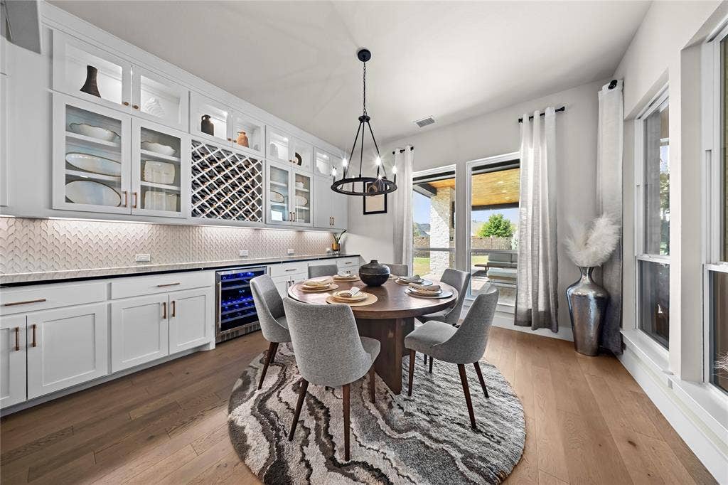 467 Mayfair Lane, Frisco, TX 75033 Built-in cabinetry with glass-front uppers, herringbone-patterned backsplash, wood-finish flooring, integrated wine refrigerator, and multiple large windows