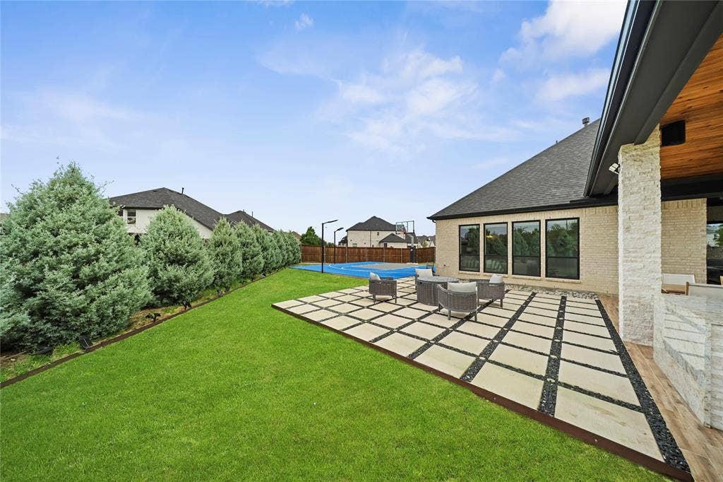 467 Mayfair Lane, Frisco, TX 75033 Expansive backyard featuring a manicured lawn, a half-court sports court, a stone-clad exterior, and a covered patio with a wood-finish ceiling