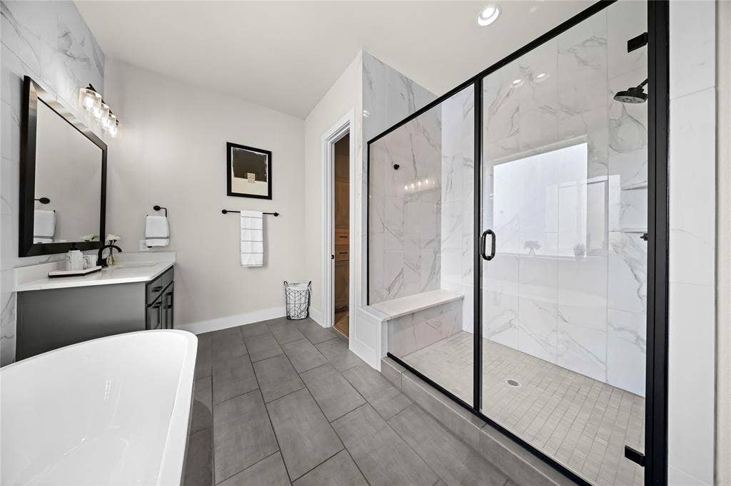 467 Mayfair Lane, Frisco, TX 75033 Freestanding soaking tub, walk-in shower with tiled walls and glass enclosure, gray floor tile, and single vanity with solid surface countertop