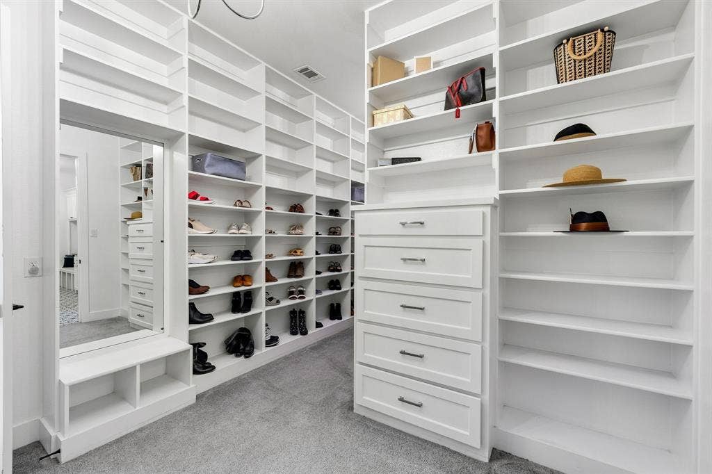 1561 Saint Peter, Prosper, TX 75078 Luxurious walk-in closet featuring extensive white cabinetry with multiple shelving units, integrated drawers, and a mirrored accent wall
