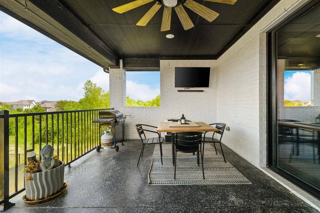 1561 Saint Peter, Prosper, TX 75078 Covered balcony featuring a ceiling fan, white brick walls, black metal railing, and a dark, textured flooring surface