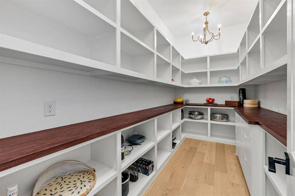 1561 Saint Peter, Prosper, TX 75078 Expansive pantry featuring extensive built-in shelving, dark wood-finish countertops, light wood-finish flooring, and an overhead chandelier