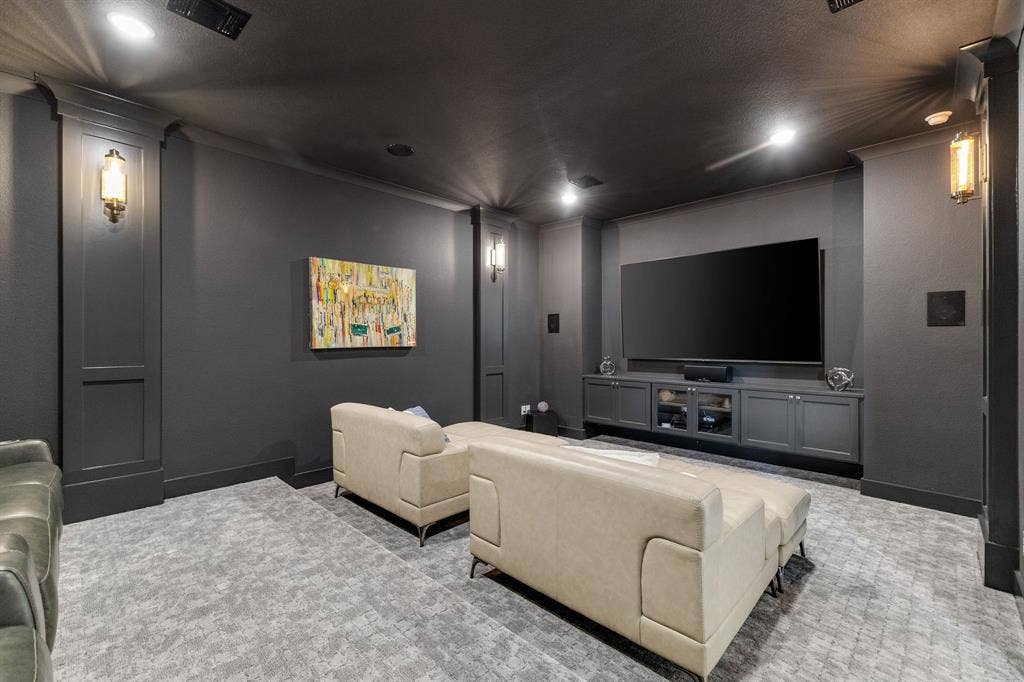 1561 Saint Peter, Prosper, TX 75078 Dedicated media room featuring a large flat-screen television mounted above built-in cabinetry, recessed lighting throughout, dark gray walls, wall-mounted sconces, plush seating areas, and patterned area flooring