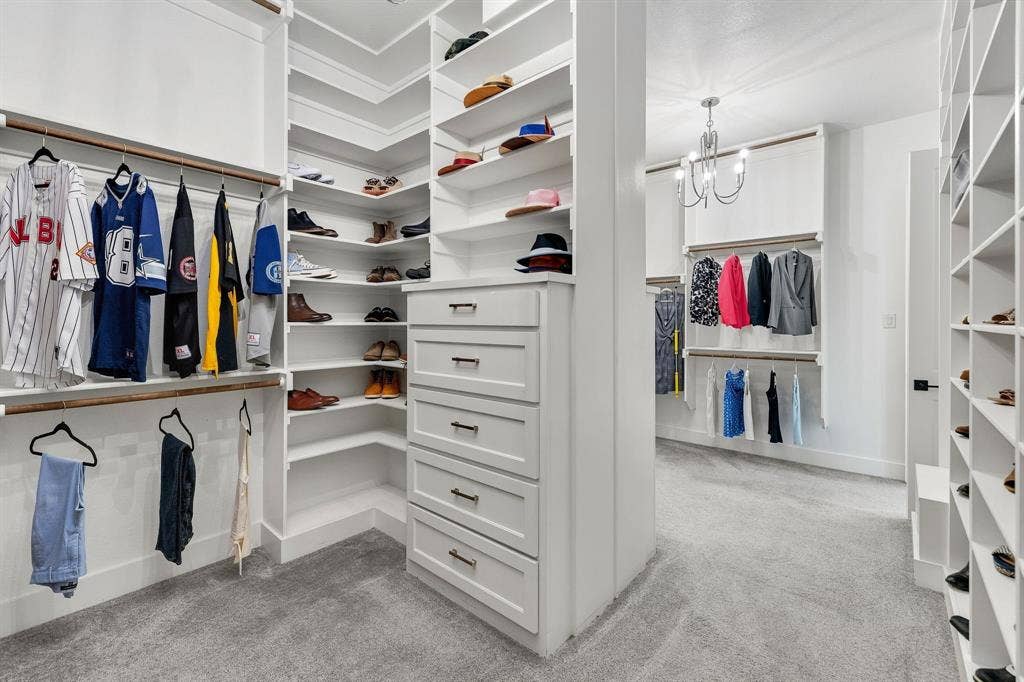1561 Saint Peter, Prosper, TX 75078 Custom built-in white shelving, integrated drawers with dark hardware, multiple hanging rods, corner shelving units, and a central chandelier