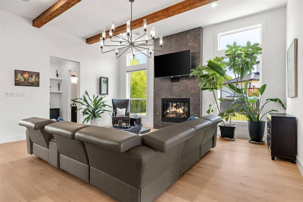 1561 Saint Peter, Prosper, TX 75078 Spacious open-concept living area anchored by a gas fireplace with dark stone surround, complemented by exposed wood ceiling beams and a modern sputnik-style pendant fixture