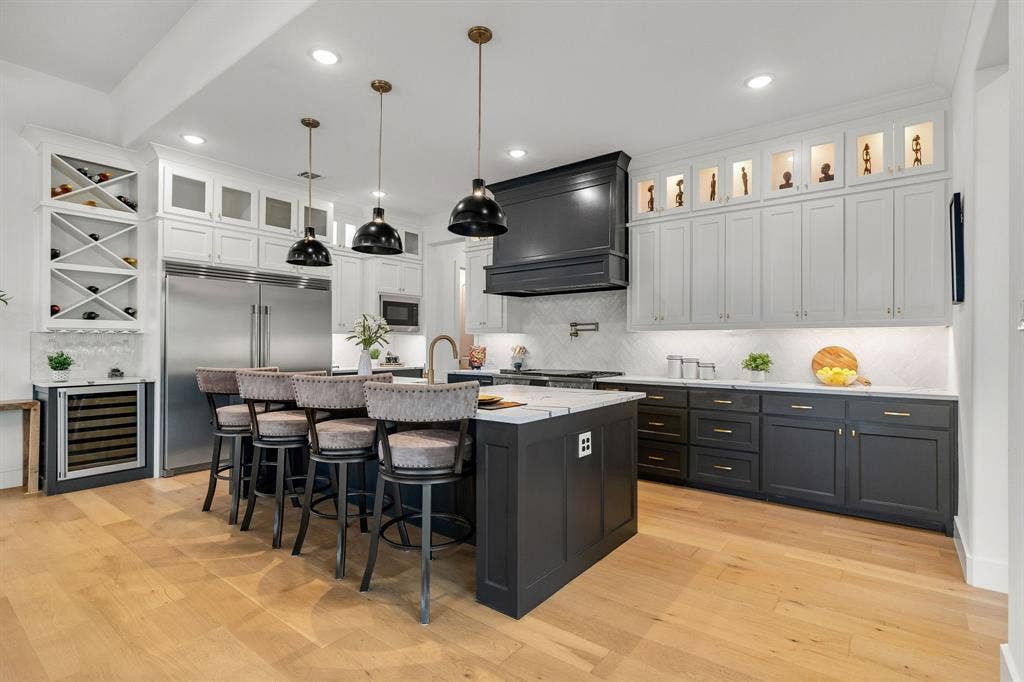 1561 Saint Peter, Prosper, TX 75078 Gourmet kitchen featuring a large central island with seating, dark shaker-style cabinetry, white upper cabinetry with glass-front accents, light wood-finish flooring, and stainless steel appliances