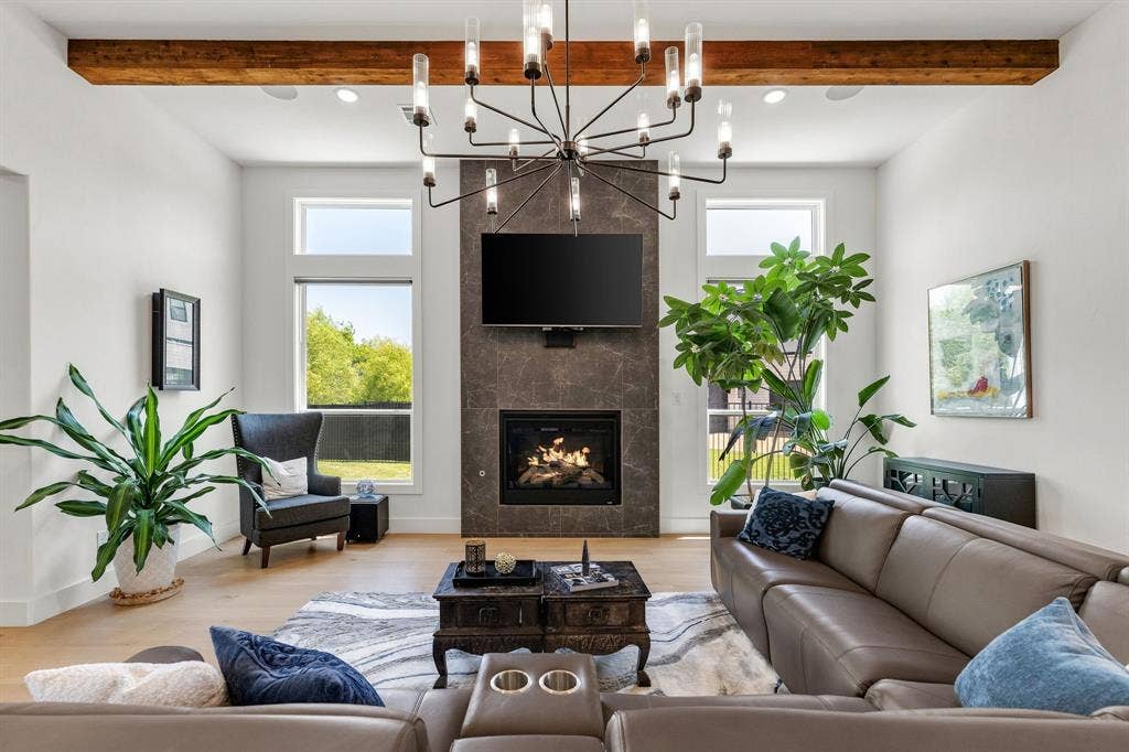 1561 Saint Peter, Prosper, TX 75078 Light wood-finish flooring, a contemporary fireplace with a dark tile surround, a linear chandelier, and exposed wood beam ceiling accents