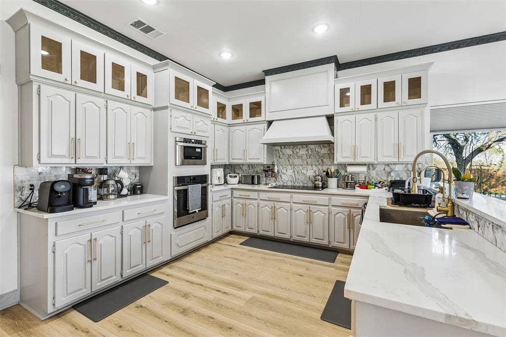 3706 Castle Drive, Rowlett, TX 75089 White cabinetry, wood-finish flooring, built-in stainless steel appliances, white countertops, and a full backsplash