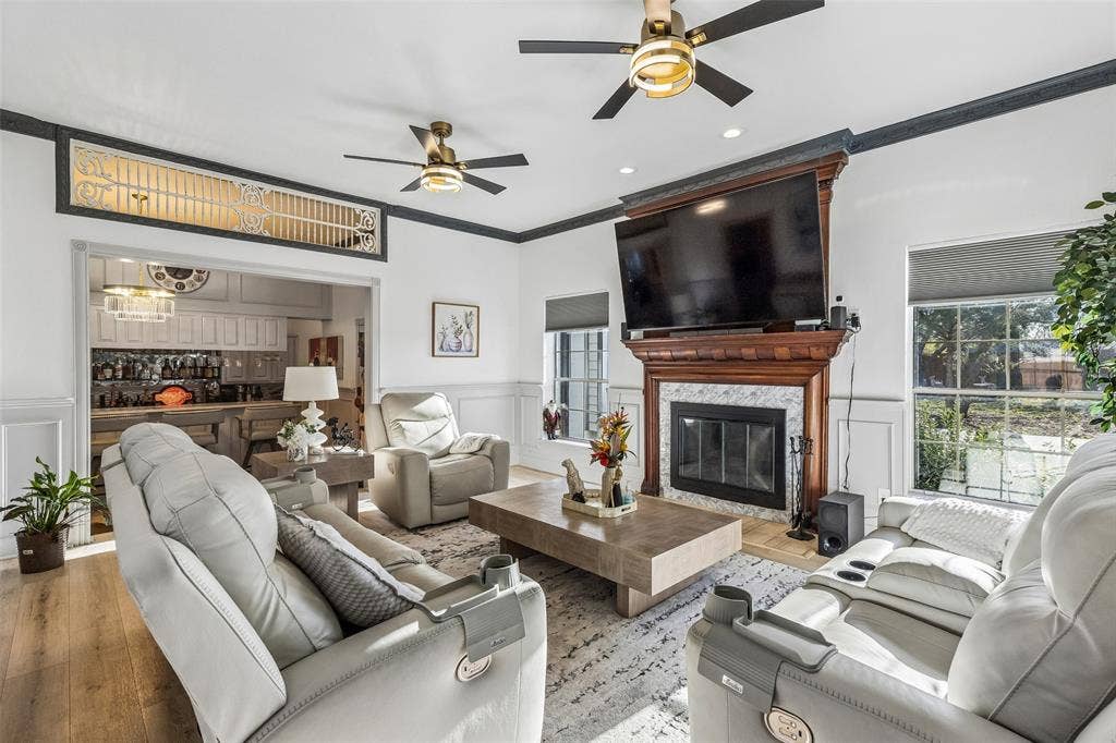 3706 Castle Drive, Rowlett, TX 75089 Living area with a wood-finish flooring, a fireplace featuring a wood mantel and stone surround, and multiple ceiling fans