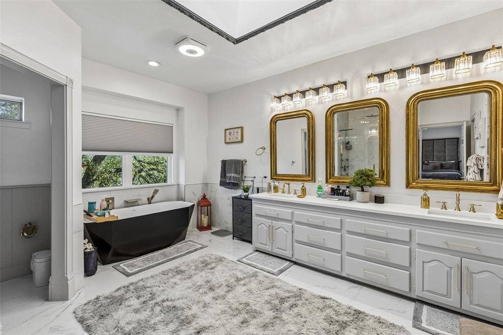 3706 Castle Drive, Rowlett, TX 75089 Freestanding soaking tub, dual vanity with two sinks, gold-framed mirrors, vanity lighting, and white tile flooring