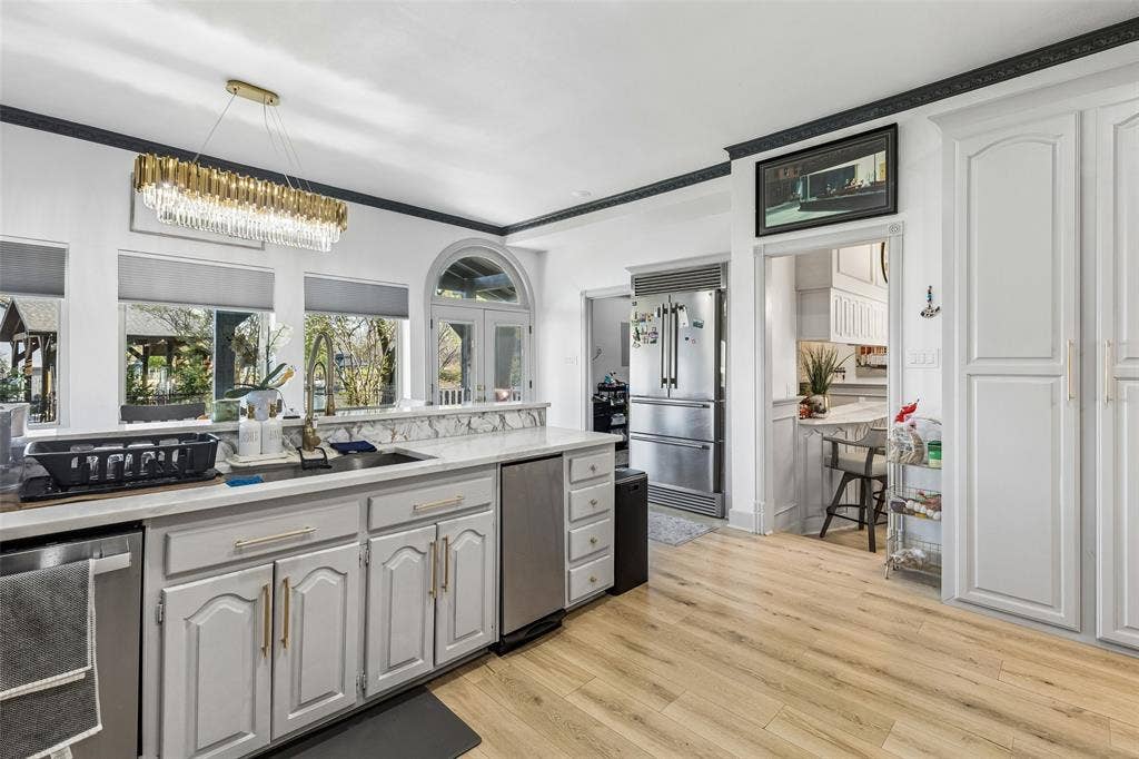 3706 Castle Drive, Rowlett, TX 75089 Kitchen featuring light wood-finish flooring, white cabinetry, integrated stainless steel appliances, a center island with sink, and a modern linear chandelier