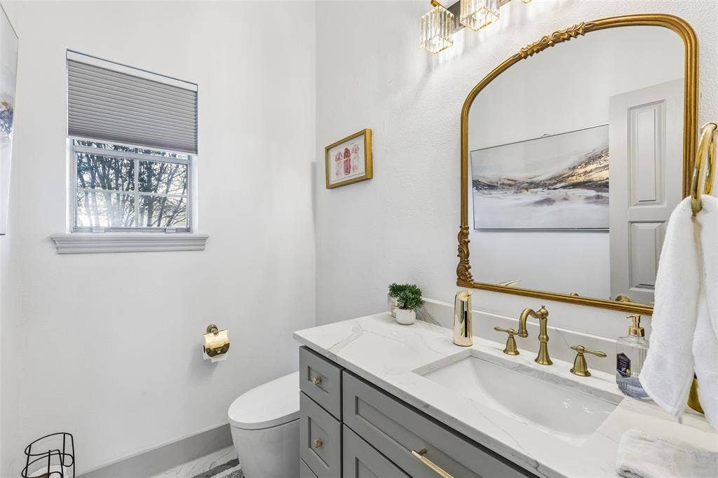 3706 Castle Drive, Rowlett, TX 75089 Vanity with a white countertop and integrated sink, brass fixtures, decorative framed mirror, and a modern light fixture