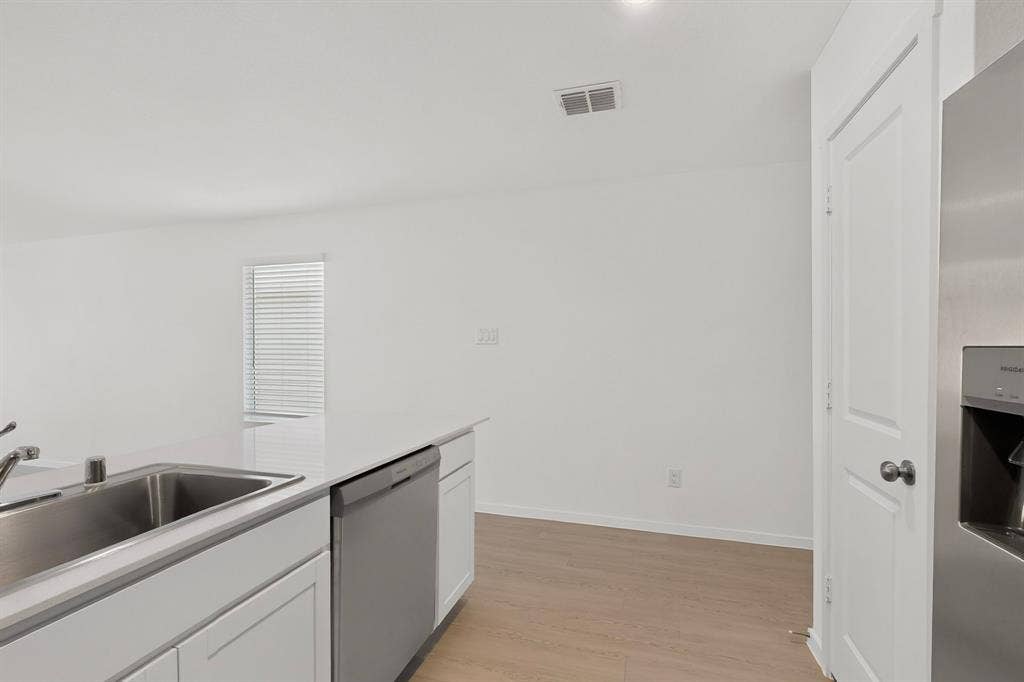 624 Kinglet Lane, Princeton, TX 75407 Kitchen island with a stainless steel sink, white cabinetry, integrated dishwasher, and light wood-finish flooring