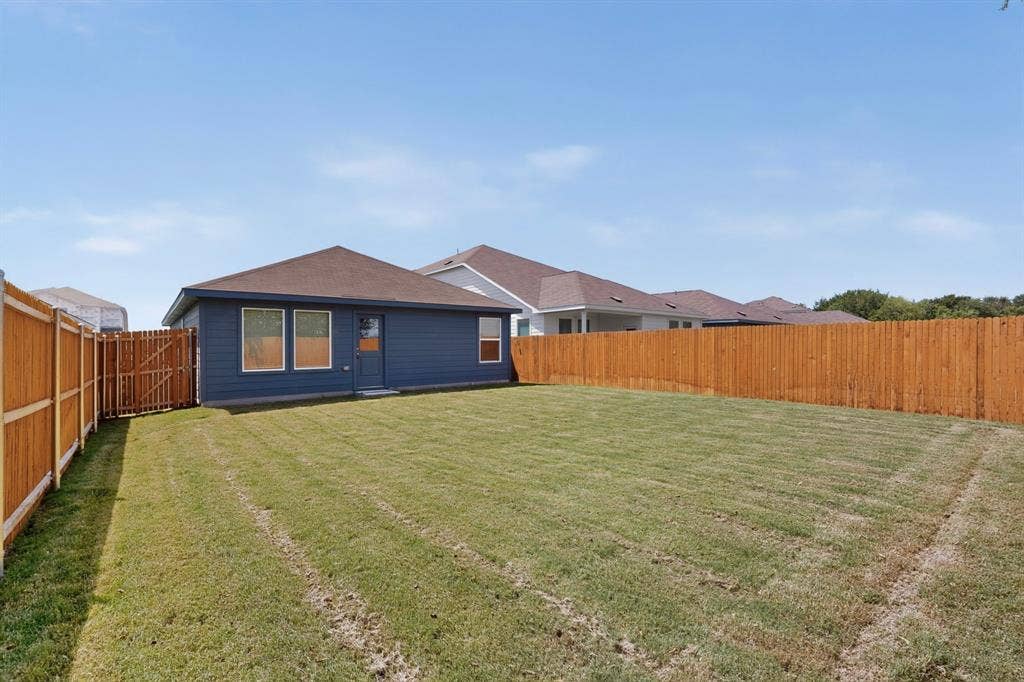 624 Kinglet Lane, Princeton, TX 75407 Expansive backyard featuring a manicured lawn, wood privacy fencing, and a rear exterior with a dark siding finish
