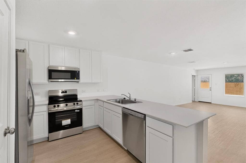 624 Kinglet Lane, Princeton, TX 75407 Kitchen featuring stainless steel appliances, white cabinetry, a kitchen island with a double basin sink, and wood-finish flooring