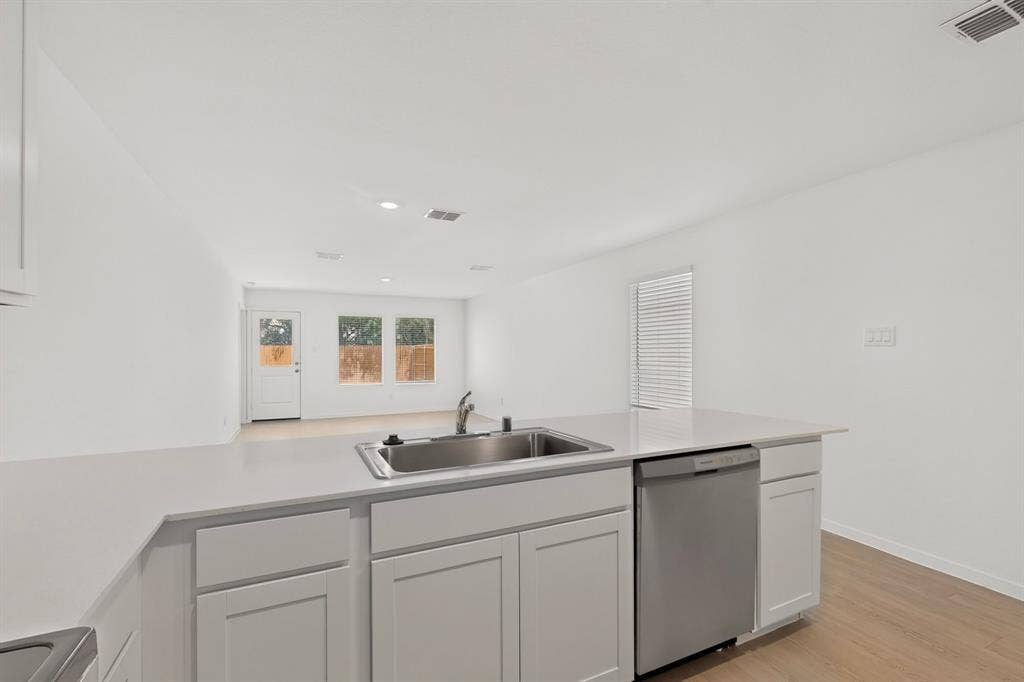 624 Kinglet Lane, Princeton, TX 75407 Central kitchen island with an undermount sink, stainless steel dishwasher, white shaker cabinetry, and light-toned countertops