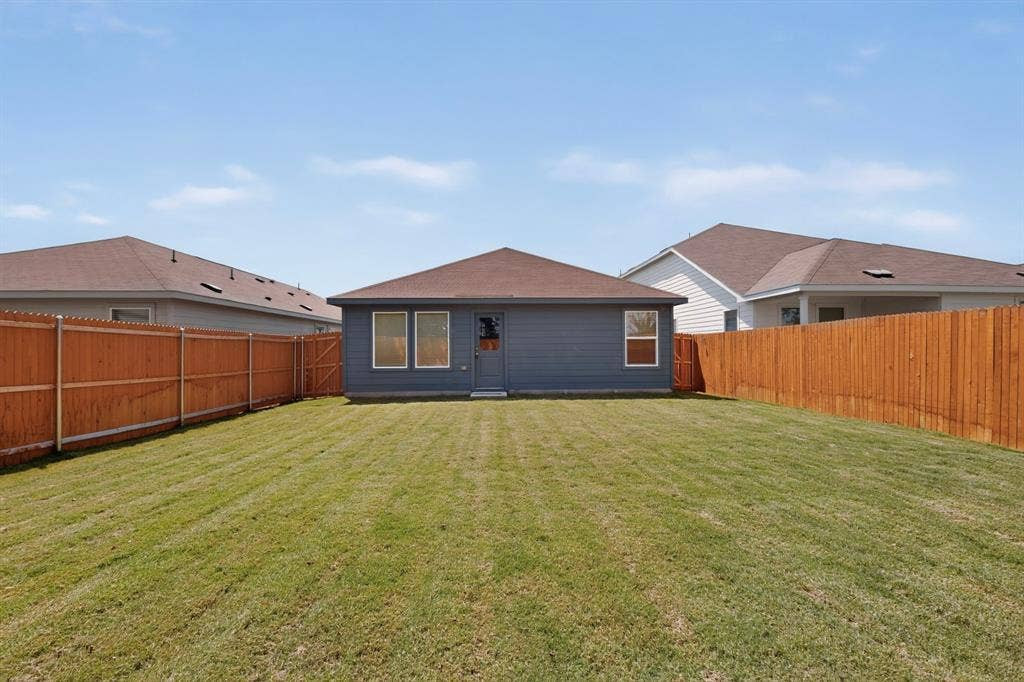 624 Kinglet Lane, Princeton, TX 75407 Expansive fenced backyard featuring a wood privacy fence, a well-maintained lawn, and a rear exterior with multiple windows