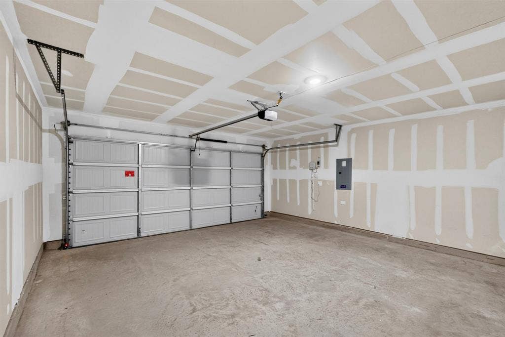 624 Kinglet Lane, Princeton, TX 75407 Spacious garage featuring a panel garage door, exposed ceiling joists, concrete flooring, and an electrical panel