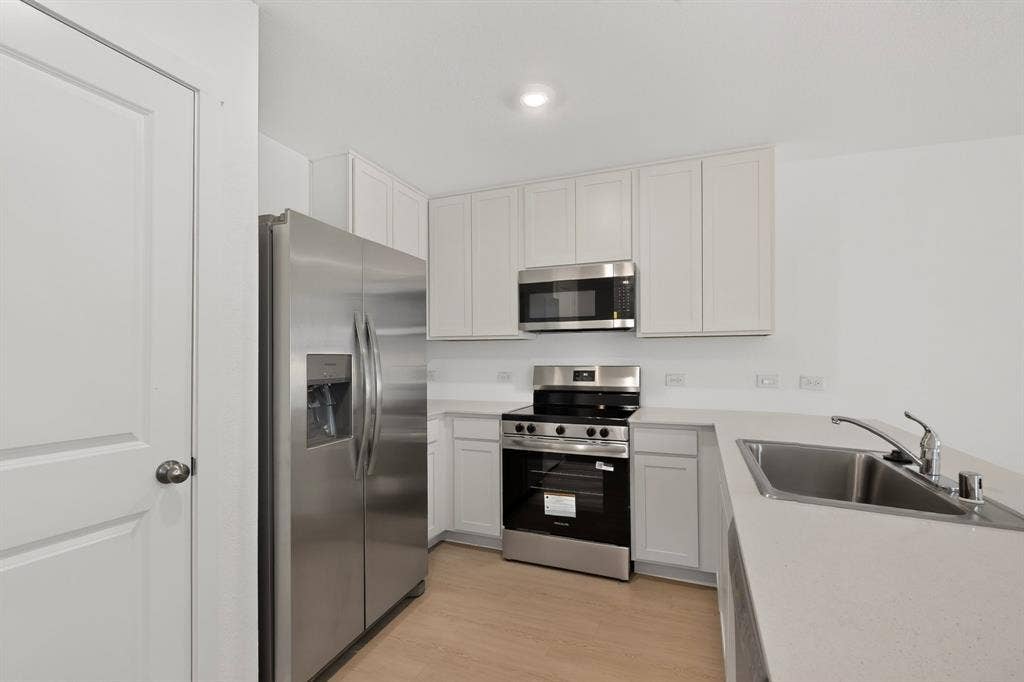 624 Kinglet Lane, Princeton, TX 75407 Contemporary kitchen featuring stainless steel appliances, light wood-finish flooring, white cabinetry, and light-toned countertops