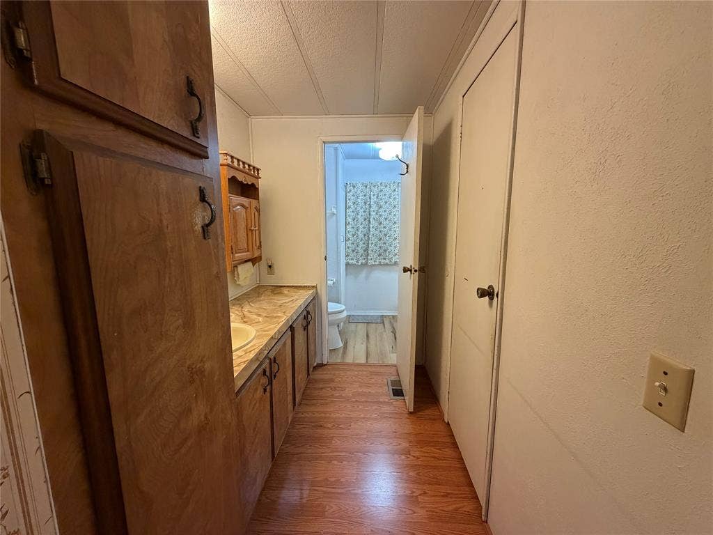 Wood-finish flooring, wood cabinetry with decorative handles, built-in vanity with integrated sink, and overhead wood storage cabinet