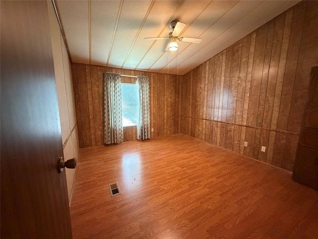 Spacious room featuring warm wood-finish flooring, wood-paneled walls, and a ceiling fan with recessed lighting