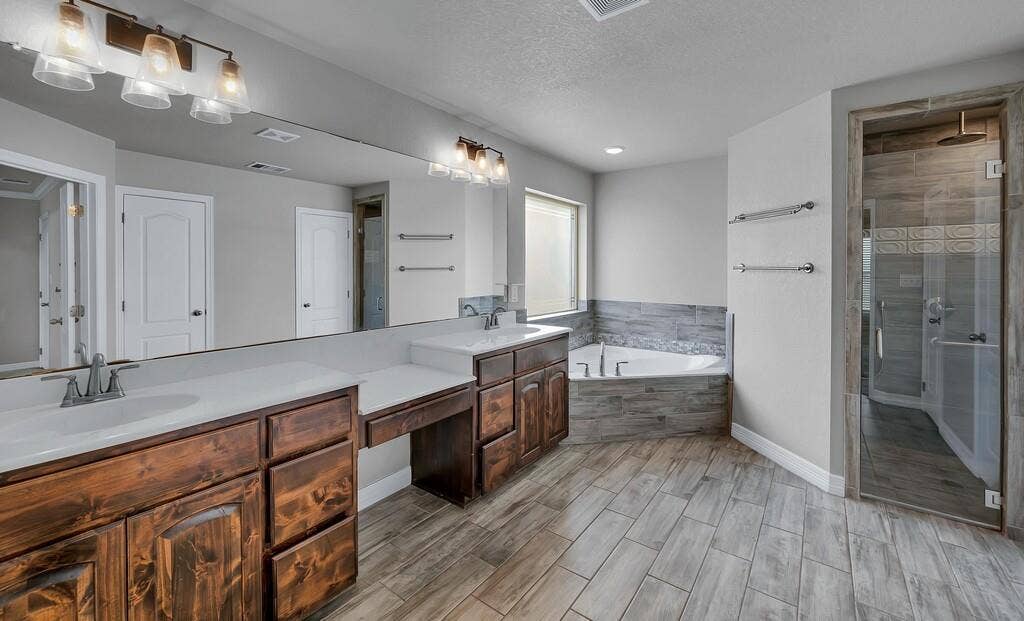 279 Sportsman Drive, Lorena, TX 76655 Dual vanities with integrated sinks, a built-in vanity station, a corner soaking tub, a separate glass-enclosed shower, and wood-finish tile flooring
