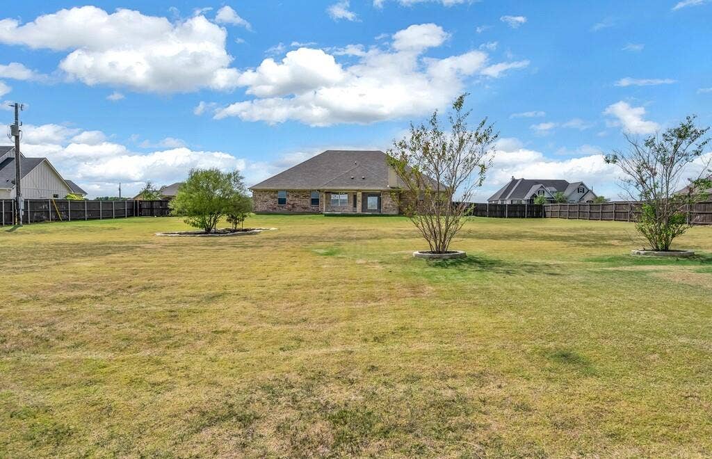 279 Sportsman Drive, Lorena, TX 76655 Expansive backyard featuring a privacy fence, mature trees, and a brick exterior dwelling with a shingle roof