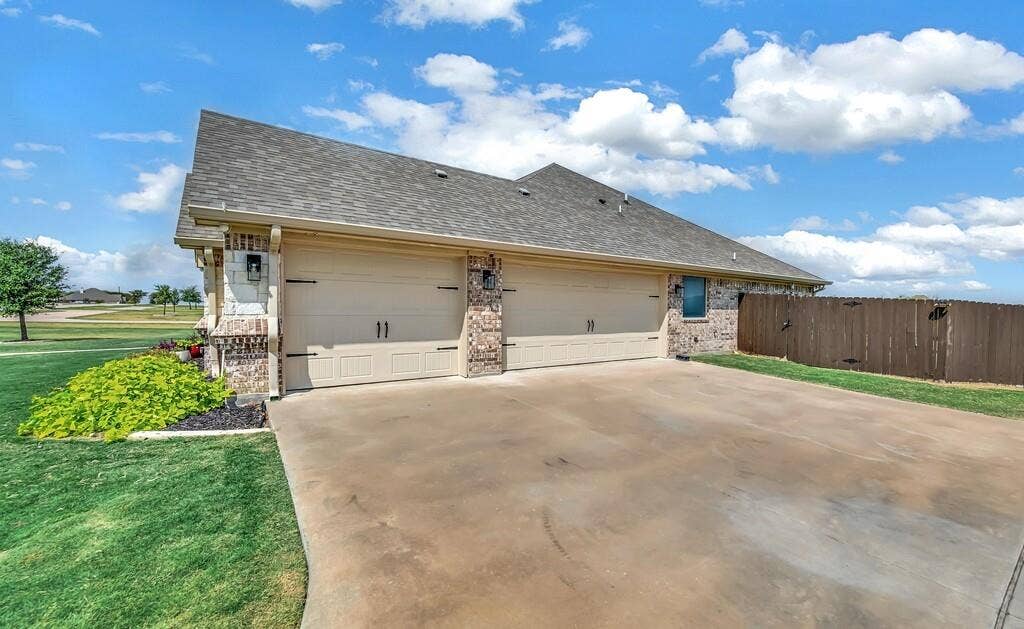 279 Sportsman Drive, Lorena, TX 76655 Three-car garage with panel doors, stone and brick facade, concrete driveway, and wood fence
