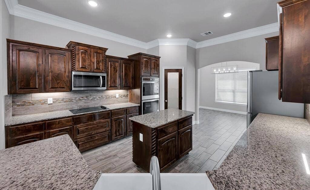 279 Sportsman Drive, Lorena, TX 76655 Kitchen featuring wood cabinetry, light-colored granite countertops, stainless steel appliances, a tile backsplash, and a central island